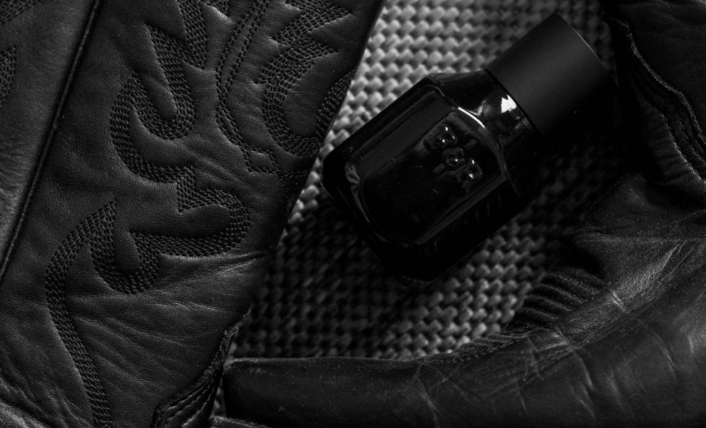 A black leather boot rests beside an elegant bottle of Fulton & Roark perfume.