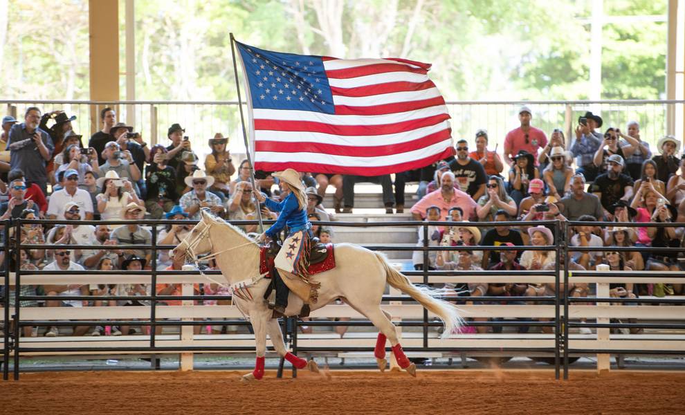 Una mujer montada a caballo sostiene una bandera estadounidense en CountryFest en Tropical Park.