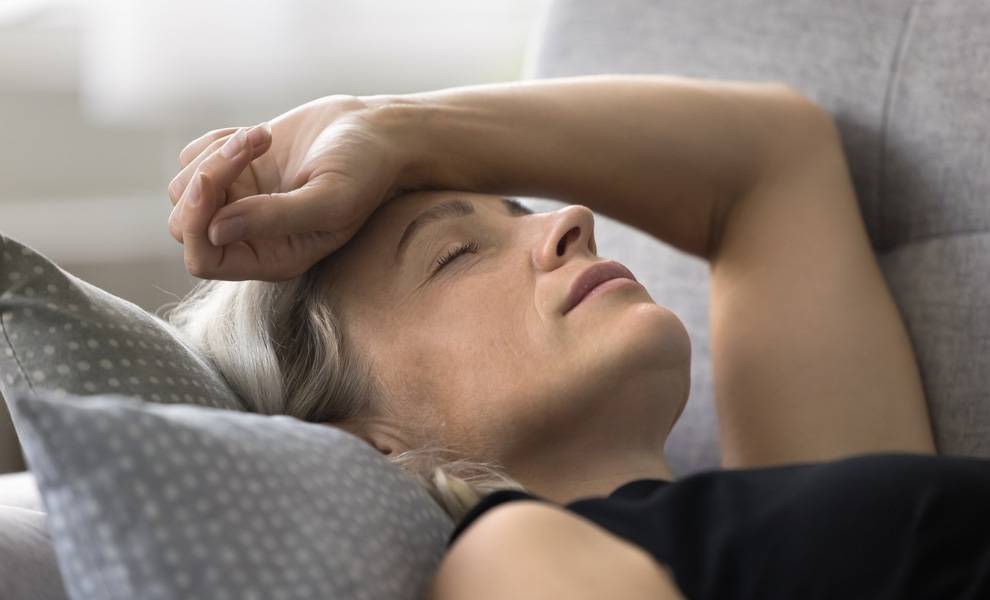 Una mujer se reclina en un sofá, apoyando la cabeza sobre una almohada, pareciendo relajada y cómoda.