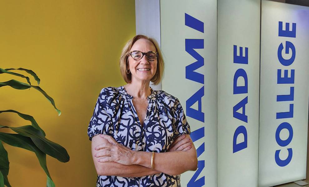 La comisionada Eileen Higgins está parada frente a un cartel que dice "Miami Dade College", sonriendo y vestida informalmente.