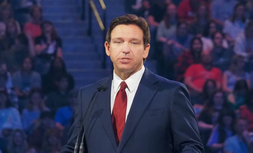 Florida Governor Ron Desantis in a suit and tie delivers a speech at a podium during a formal event.