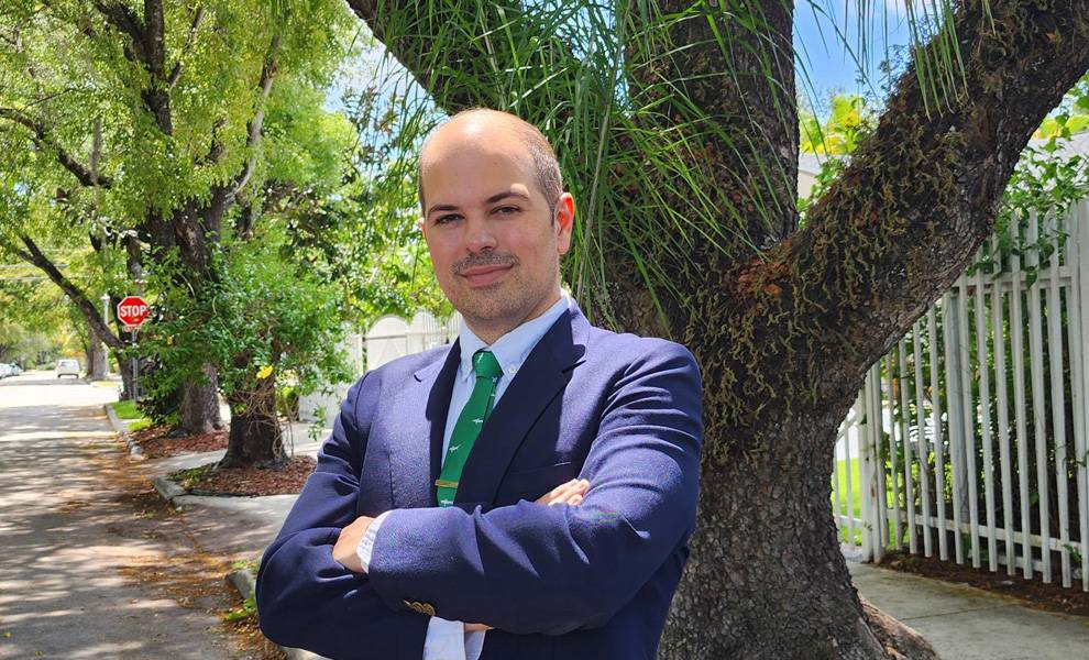 Jose Francisco Regalado, con traje y corbata verde, se encuentra con confianza frente a un gran árbol.