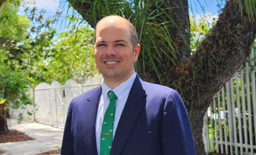 Jose Francisco Regalado in a suit and green tie stands confidently in front of a large tree.