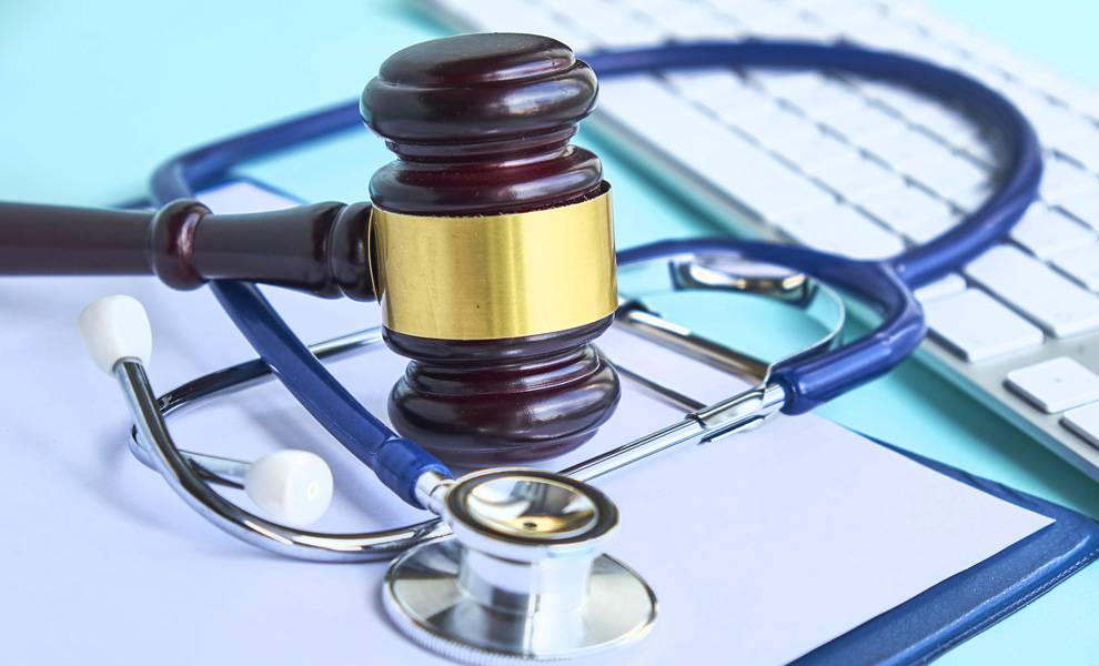 Un mazo y un estetoscopio descansan sobre un escritorio junto a un teclado y un cuaderno, simbolizando una mala praxis médica.