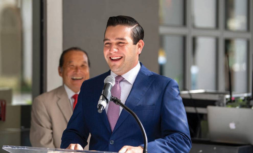 Un hombre con traje y corbata sonríe con confianza en un podio durante una conferencia.