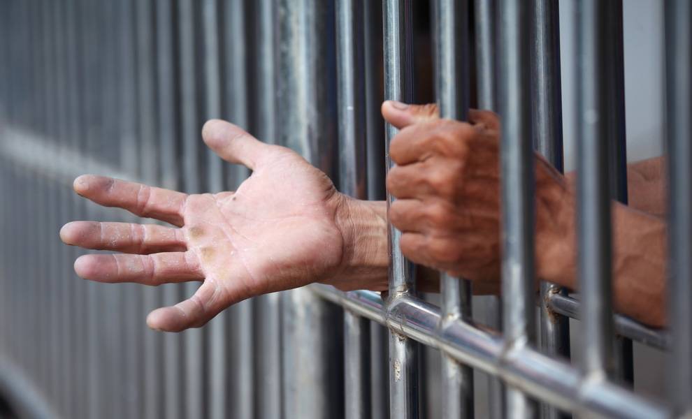 Prison bars with a persons hands reaching out.
