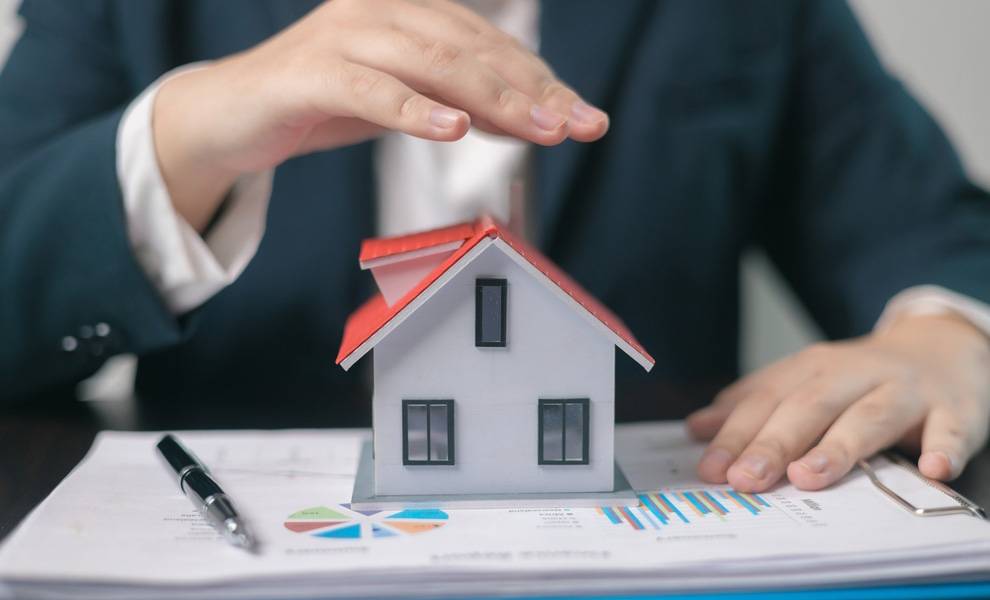Una persona sostiene su mano sobre una casa pequeña para representar la cobertura de seguro para su hogar.