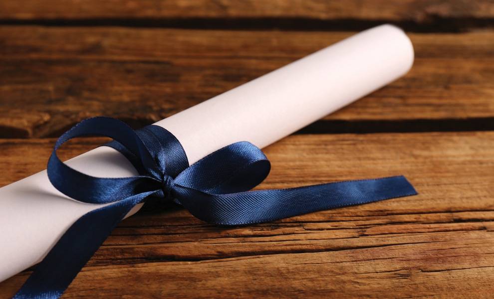 Un diploma envuelto en un lazo azul encima de un escritorio.