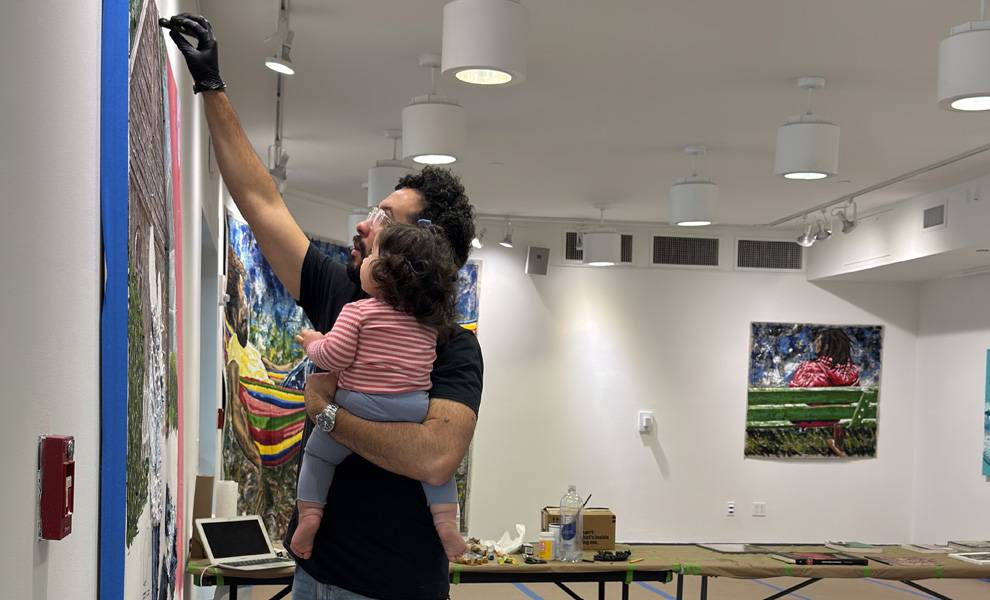 William Osorio painting on a canvas while holding his daughter.