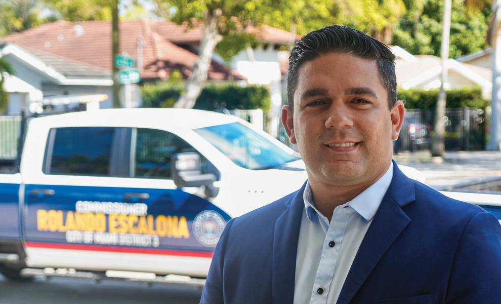 El comisionado Rolando Escalona viste un traje azul y al fondo se ve una camioneta blanca.