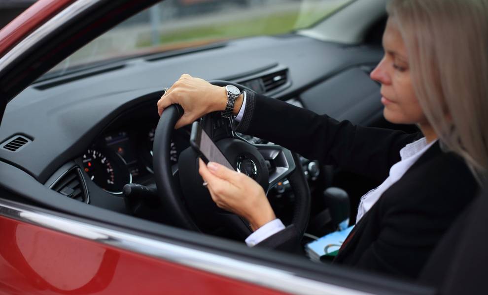 A woman in a red car using her cell phone while driving.
