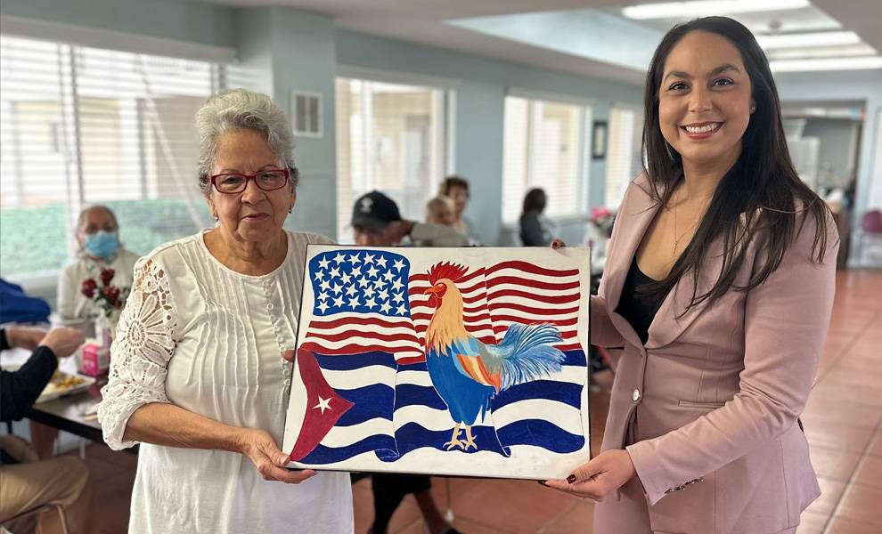 Commissioner Natalie Milian Orbis holding a painting of an American and Cuban flag with a Miami resident.