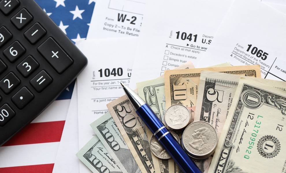 Tax forms, money and a pen sitting on top of an American flag.