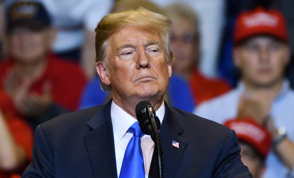 El presidente Donald Trump, con un traje oscuro y una corbata azul brillante, se encuentra en un podio hablando por un micrófono.