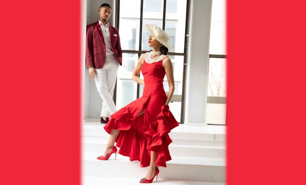 Yli Liriano lleva un vestido rojo, y al fondo se ve a un hombre con un traje blanco y una chaqueta roja.