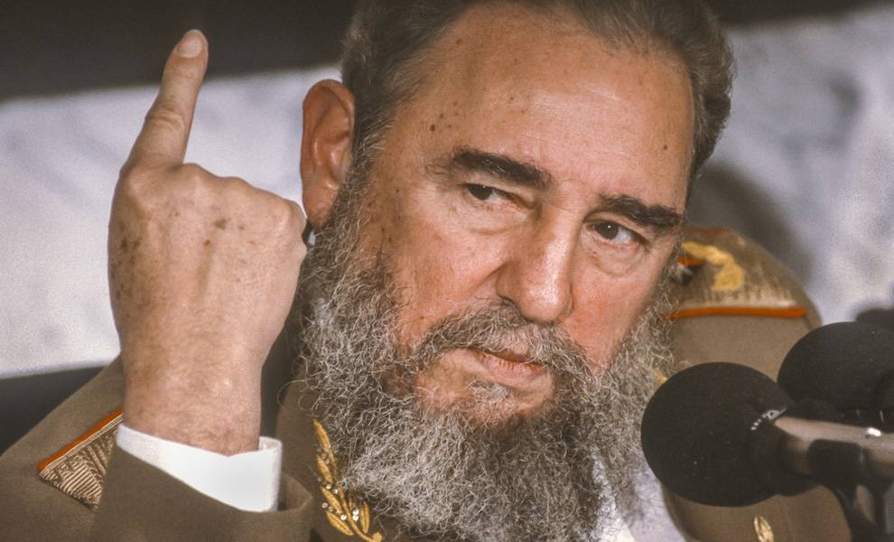 Fidel Castro, con una tupida barba gris y uniforme militar, habla ante unos micrófonos, levantando un dedo hacia arriba mientras expone un punto. Su expresión es seria y concentrada, lo que sugiere que se dirige a una audiencia o a la prensa.
