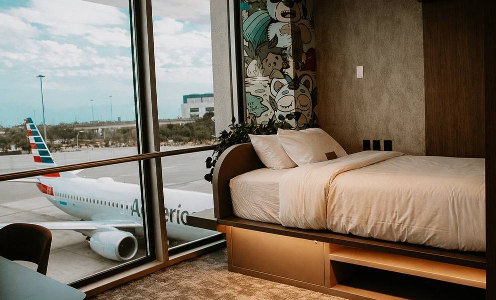 A modern airport hotel-style room at MIA features a neatly made bed positioned beside a large floor-to-ceiling window.