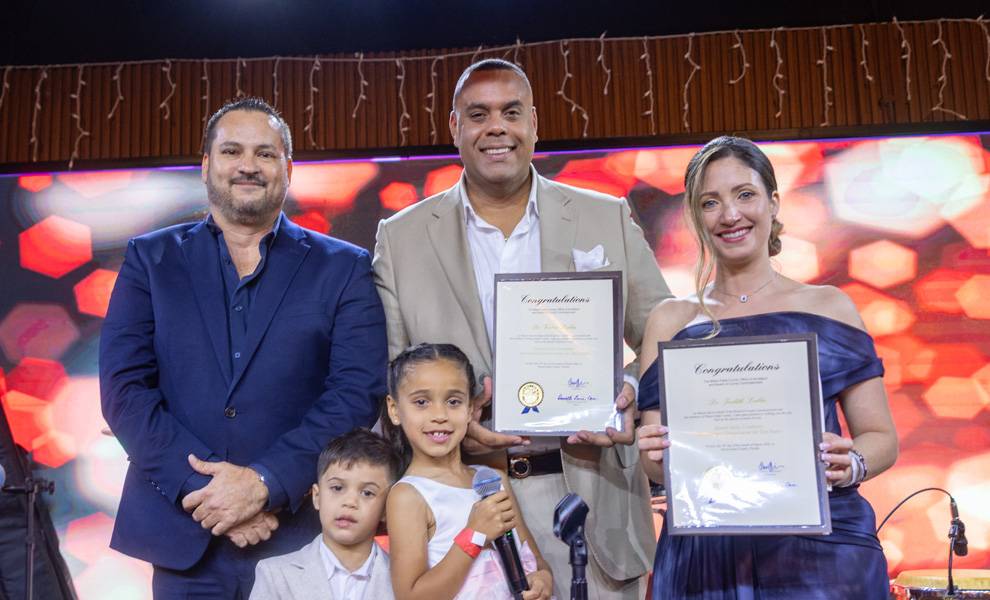 Dos hombres, una mujer y dos niños permanecen de pie sobre un escenario durante una entrega de premios en el evento de Sunset Smile Creations.