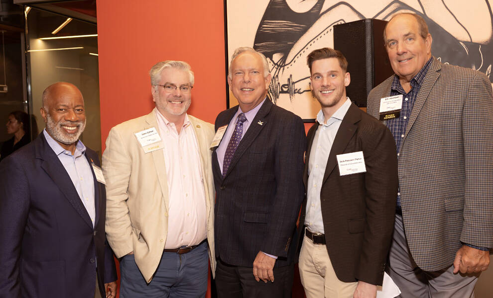Five professionally dressed men stand together at a Care Resource event, smiling at the camera.