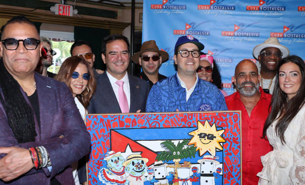 A group of attendees pose together at a “Cuba Nostalgia” event, smiling in front of a branded backdrop while holding a colorful artwork featuring Cuban-inspired imagery.