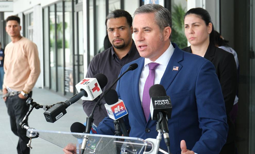 Close-up of Miami-Dade Tax Collector Dariel Fernandez speaking into microphones at a press conference about accountability, with several people standing behind him outside a building.