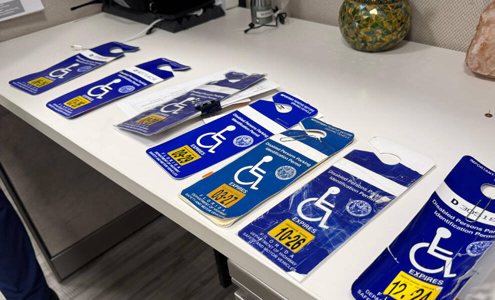 A close-up of multiple blue disabled parking placards laid out on a desk, each displaying the wheelchair accessibility symbol and expiration dates.