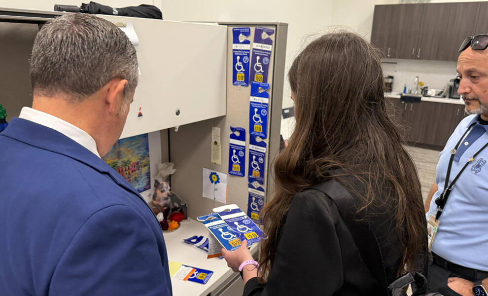 Miami-Dade Tax Collector Dariel Fernandez and others stand in an office cubicle reviewing disabled parking placards.