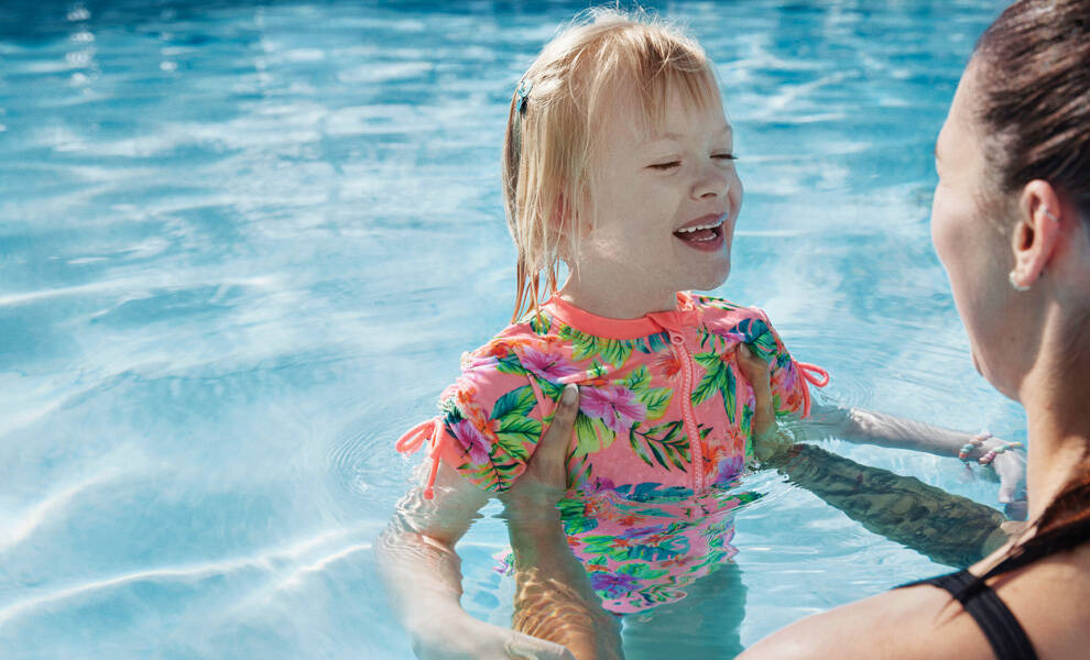 Aetna autism support image featuring a young child smiling during a swim therapy session while being assisted by an adult in a pool.