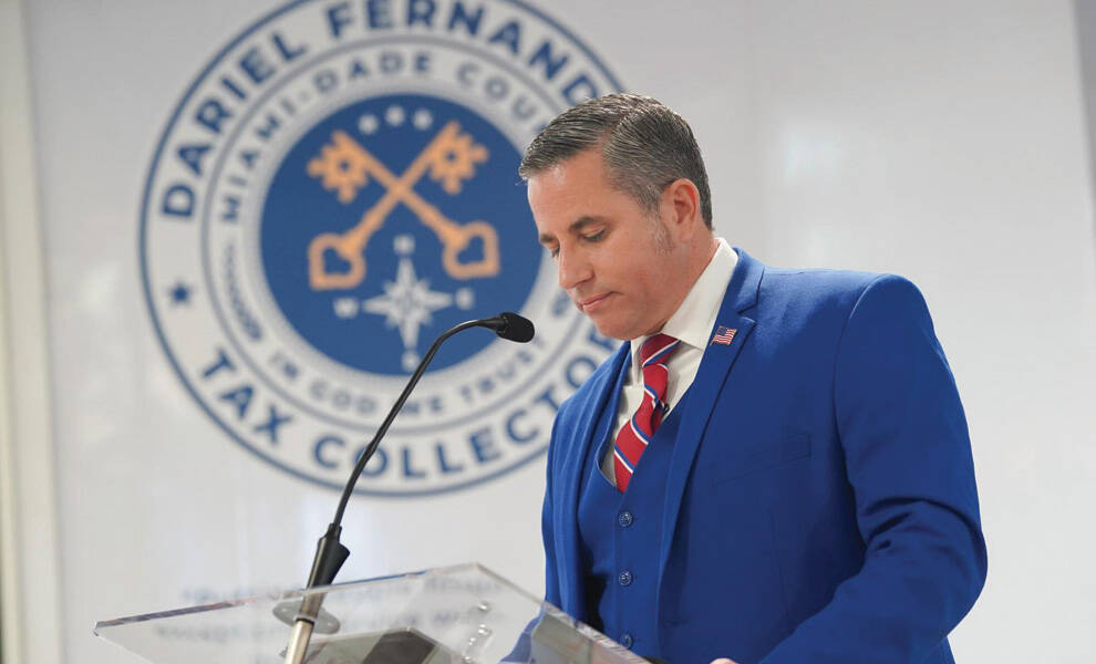 Dariel Fernandez speaks at a podium in front of the Miami-Dade County Tax Collector's Office seal during a formal announcement or public event.