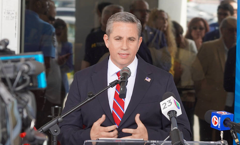Miami-Dade County Tax Collector Dariel Fernandez speaks at a public event podium surrounded by microphones and media cameras during a press conference.