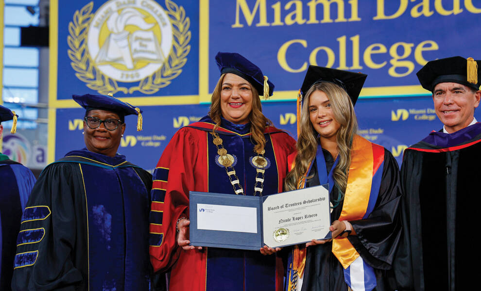 Un graduado del Miami Dade College recibe un certificado de beca de la Junta de Fideicomisarios mientras posa con administradores y miembros del cuerpo docente de la institución durante una ceremonia de graduación.