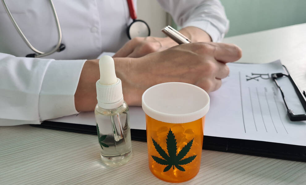 Un profesional de la salud escribe en un portapapeles de recetas, junto a un frasco de aceite de CBD y un envase de medicamentos con el símbolo de una hoja de cannabis, lo que representa un tratamiento con marihuana medicinal y una consulta médica.