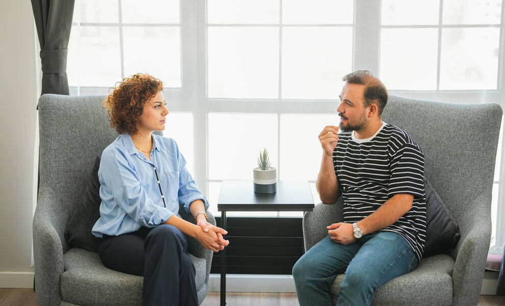 Aetna mental health consultation featuring a woman and man seated in armchairs during a counseling session in a bright office setting, discussing emotional wellness and support.
