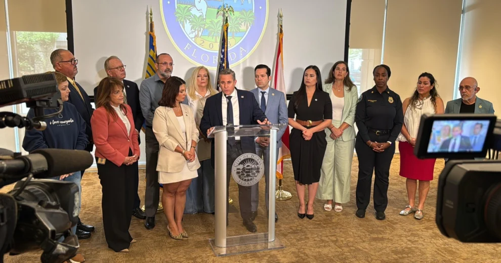 El recaudador de impuestos del condado de Miami-Dade, Dariel Fernandez, habla desde un podio durante una conferencia de prensa en la que se anuncia una iniciativa de ayuda humanitaria para las víctimas del terremoto en Venezuela. Está acompañado por funcionarios locales, líderes comunitarios, personal de primera respuesta y representantes de organizaciones sin fines de lucro que se encuentran detrás de él.