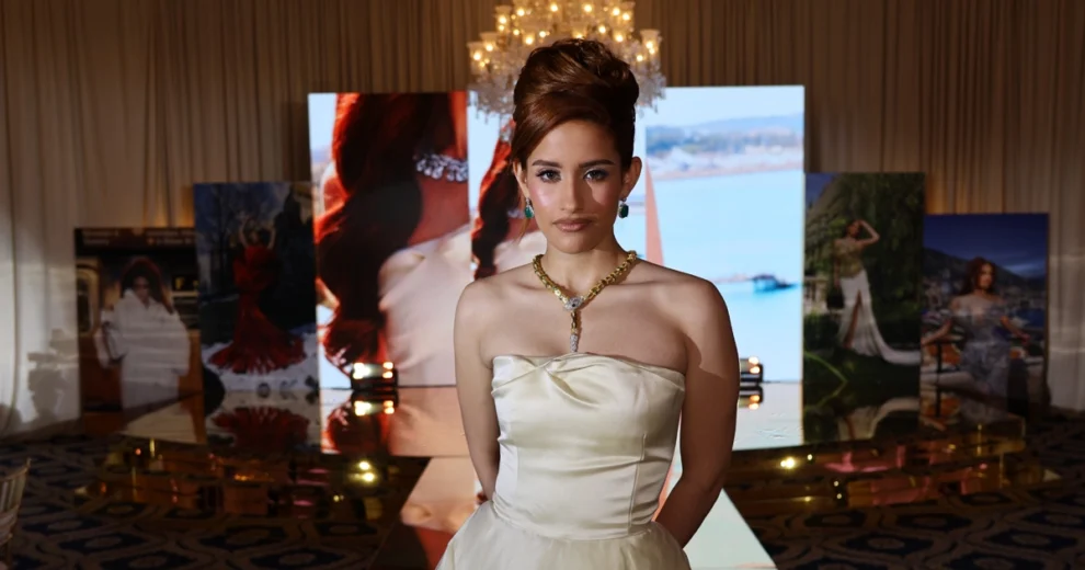 Leah Reyes Amores se encuentra al final de una pasarela, luciendo un elegante vestido color marfil sin tirantes, con corpiño ajustado y falda vaporosa.