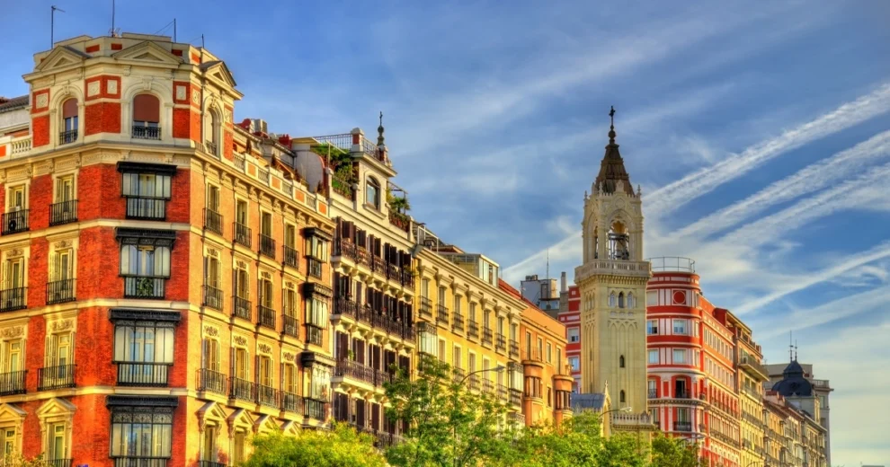 Colorful streetscape in central Madrid featuring historic multi-story buildings with decorative facades, wrought-iron balconies, and large windows.