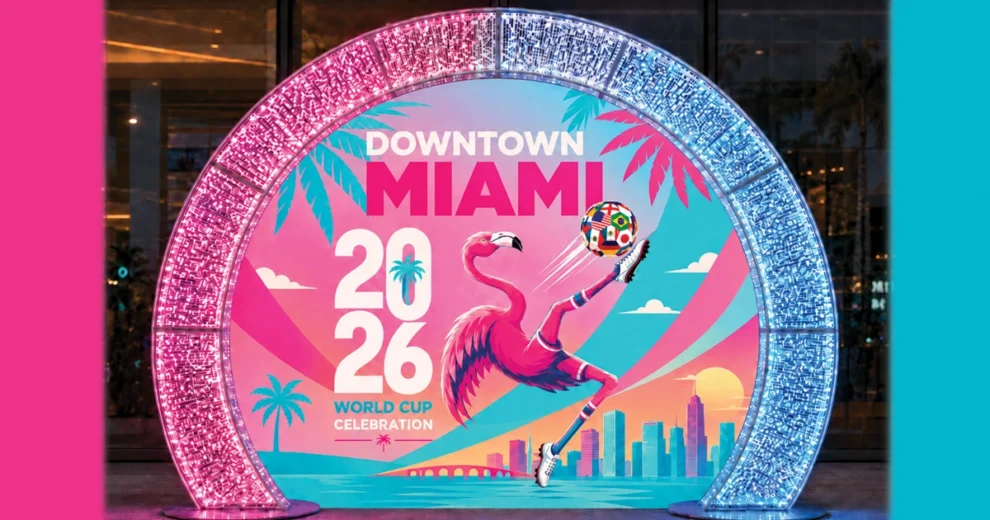 Una vibrante instalación titulada "Celebración de la Copa Mundial 2026 en el centro de Miami" presenta un flamenco rosa que equilibra un colorido balón de fútbol, ​​con un telón de fondo de palmeras, vistas al océano y el horizonte urbano de Miami. Unos arcos iluminados en rosa y azul enmarcan la instalación, creando un escenario festivo ideal para tomar fotografías y celebrar la Copa Mundial de la FIFA 2026.