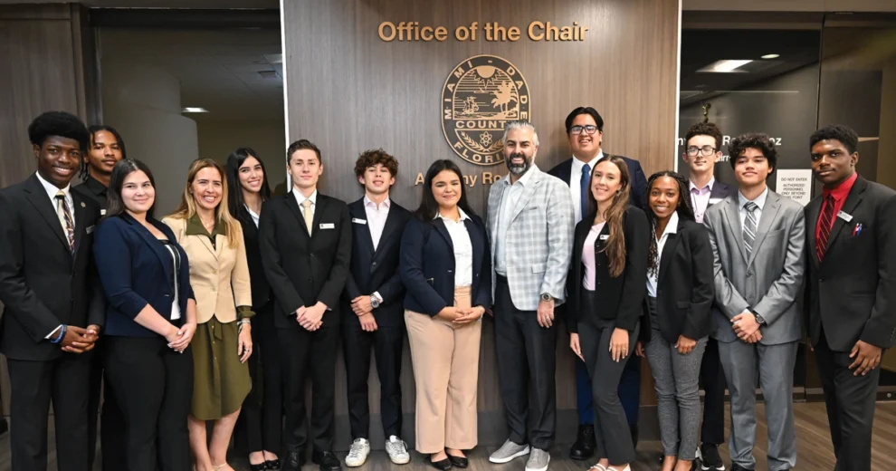 Participants in the Miami-Dade Youth Engagement Program pose with county leaders inside the Miami-Dade County Office of the Chair. The group stands in front of the county seal and office signage, smiling for a commemorative photo.