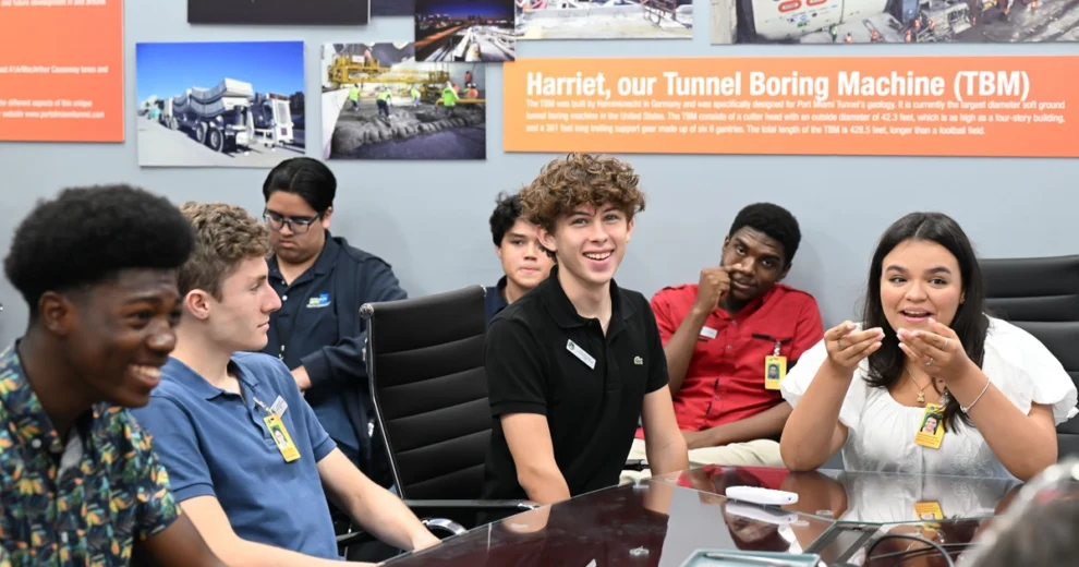 Chairman Anthony Rodriguez Announces the Return of the Youth Engagement Program for 2026 — Applications Now Open for High School Students 2 Students participating in the Miami-Dade Youth Engagement Program engage in a group discussion around a conference table during an educational visit, with infrastructure project displays visible in the background.