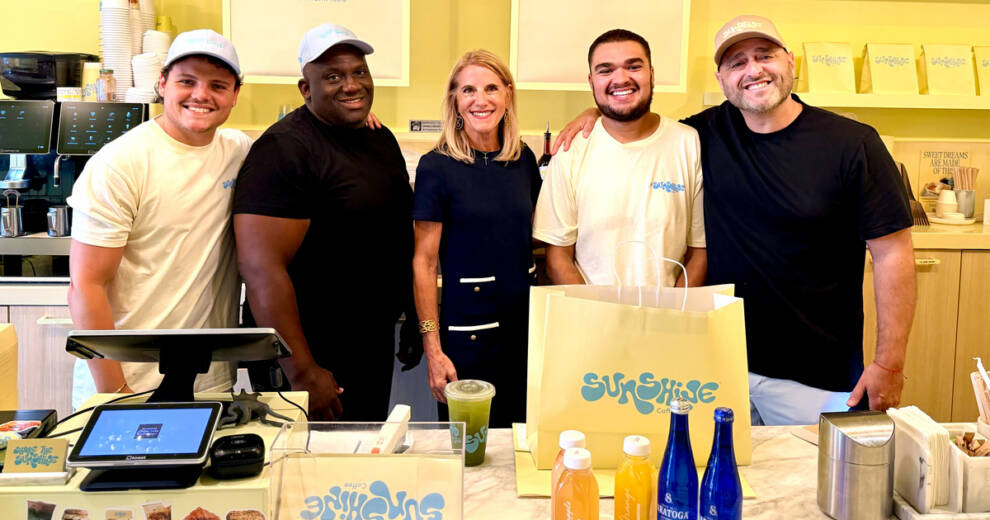 La comisionada Vicki Lopez lanza el programa de subvenciones para pequeñas empresas familiares de 2026 para emprendedores del Distrito 5 1 La comisionada del condado de Miami-Dade, Vicki Lopez, posa detrás del mostrador junto a cuatro empleados en el interior de una cafetería luminosa y moderna.
