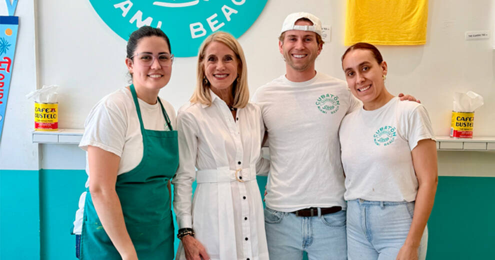 La comisionada del condado de Miami-Dade, Vicki Lopez, está junto a tres empleados dentro de una colorida cafetería.