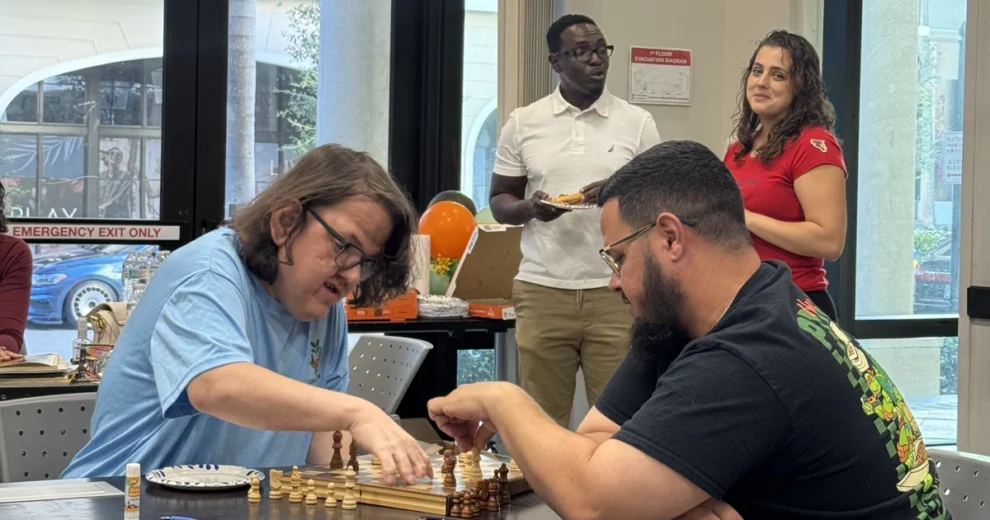 Two participants concentrate on a game of chess during an ACES community event while other attendees socialize in the background.