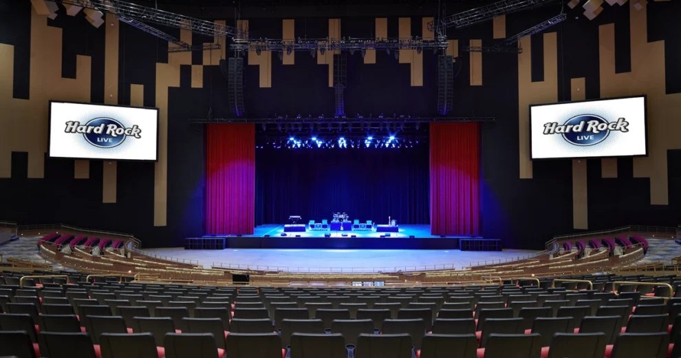Wide interior view of Hard Rock Live at Seminole Hard Rock Hotel & Casino Hollywood, showing the empty theater with rows of seats facing a brightly lit stage framed by red curtains.