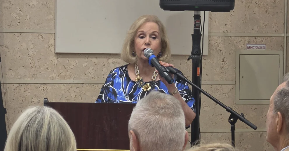 Luis Manuel Otero Alcántara Documentary Screening Opened Miami Series on Censored Cuban Artists 1 Aida Levitan speaks at a podium into a microphone during a public event, addressing an audience in a conference room. She wears a blue patterned blouse and a statement necklace while delivering opening remarks.