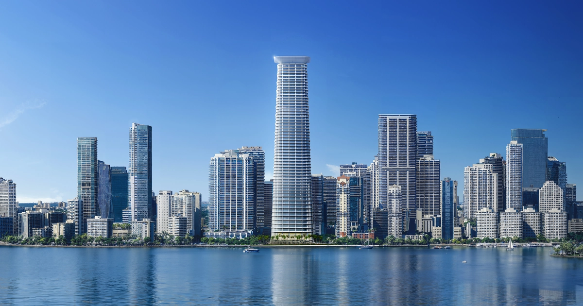 A panoramic daytime view of a modern Miami waterfront skyline, with numerous high-rise residential and office buildings along the water under a clear blue sky. Several boats are visible in the foreground.