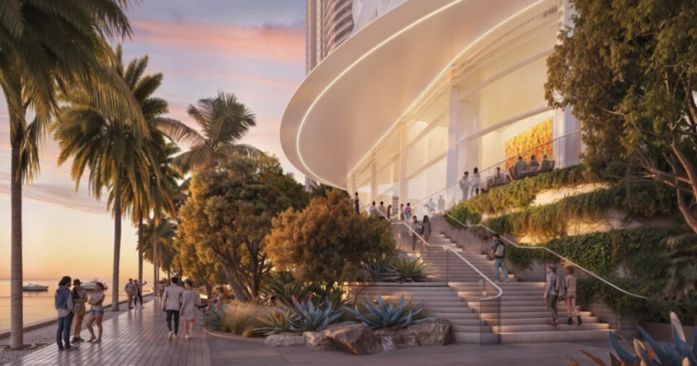 Architectural rendering of the planned Citadel headquarters in Miami, showing a modern curved white building along the waterfront with landscaped terraces, palm trees, pedestrian walkways, and people enjoying the waterfront at sunset.
