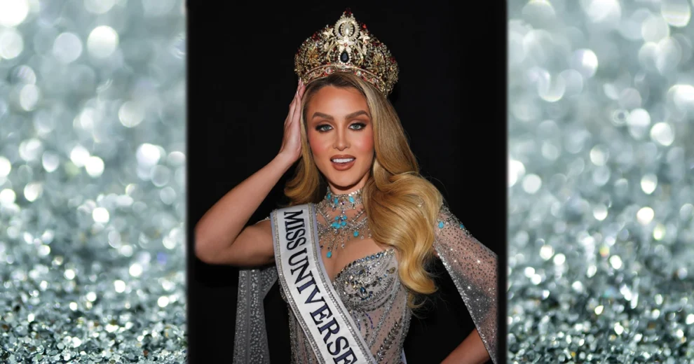 Miss Universe Cuba Mia Dio poses wearing her crown and sash, dressed in a sparkling silver gown and jewelry against a glittering backdrop.
