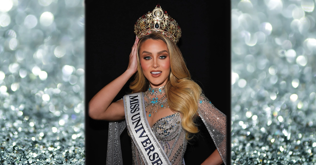 Miss Universe Cuba Mia Dio poses wearing her crown and sash, dressed in a sparkling silver gown and jewelry against a glittering backdrop.