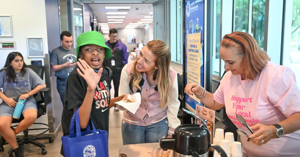 La comisionada del condado de Miami-Dade, Raquel Regalado, sonríe e interactúa con un joven visitante que lleva un sombrero de pescador de color verde brillante durante un evento comunitario.