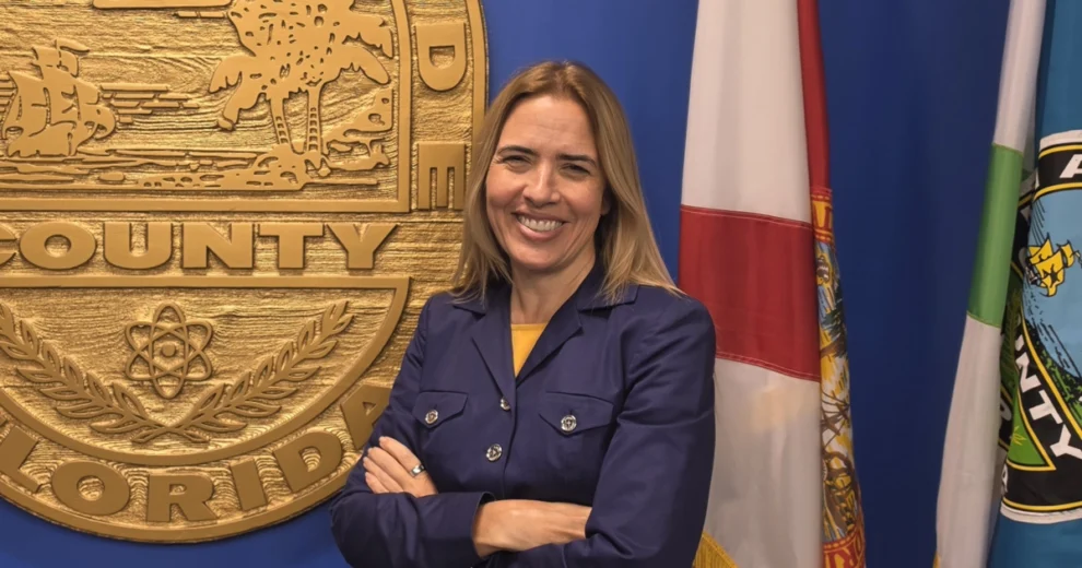 Comisionada Raquel Regalado: Liderando Miami-Dade a través de la inclusión, la innovación y el impacto comunitario 1 La comisionada del condado de Miami-Dade, Raquel Regalado, posa sonriente y con los brazos cruzados frente al sello y las banderas del condado de Miami-Dade, vistiendo una chaqueta azul marino sobre una blusa amarilla.